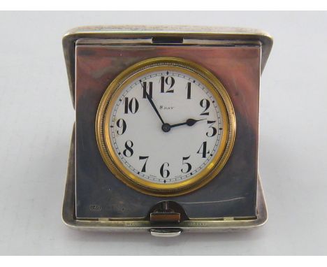 A folding silver travelling clock with eight day movement and black numerals on the white enamel dial, the case engine turned