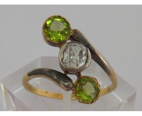 A diamond and peridot ring, the central cushion cut approx. 0.45 carat, between two obliquely set round cut peridots, the yel