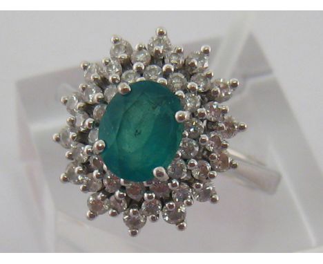 An emerald and diamond cluster ring, the central oval cut stone approx. 0.9 carat, in a two row surround of brilliants totall