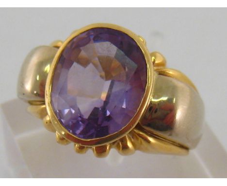 An Italian 18 carat gold and amethyst dress ring, the oval cut stone approx. 12mm long, rub over set in a gadrooned mount, th