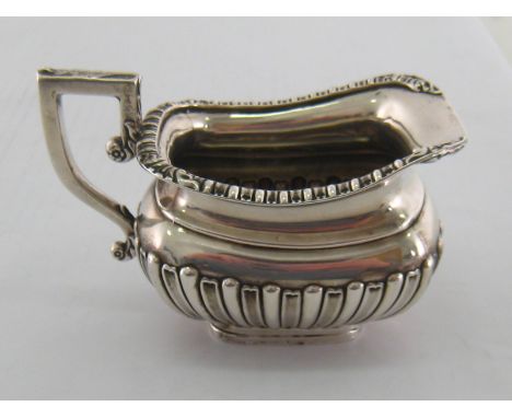 A silver cream jug of half ribbed barge shape with decorated stiffening rim and leaf capped handle. Birmingham, 1902 and broa