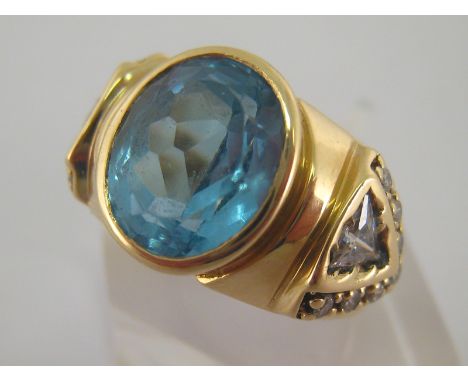 A 14 carat yellow gold and blue topaz dress ring, the central oval cut stone 10.6mm long, to white stone set shoulders, the s