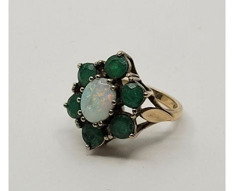 A 9ct. gold, emerald and opal dress ring, set oval cabochon opal to centre (stone with chip and fracture line), bordered by s