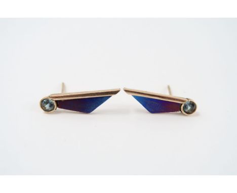 A pair of unusual earrings, in the form of a stylised wing, titanium and gold, each set with a round bright blue stone, 2cm l