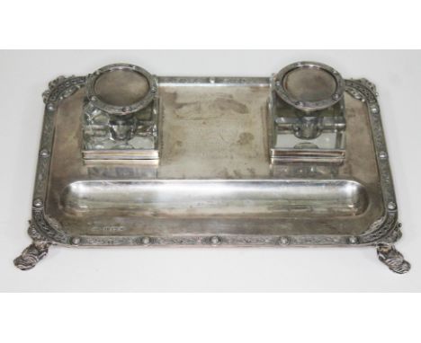 A presentation silver inkstand, with two square glass inkwells on base with Celtic border and four mythical feet, inscribed '