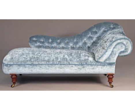 A Victorian-style chaise lounge with buttoned back and scroll support, upholstered in light blue velvet-type material, on tur