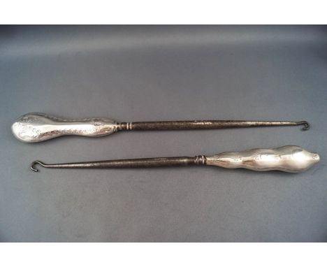 Two large silver handled button hooks, each with a shaped wavy handle, one of which engraved with a ribbon tied bow and flora