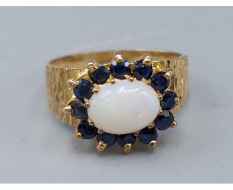 A 9ct gold ring set with a Cabochon Opal surrounded by Sapphire, 3.8gms, ring size P