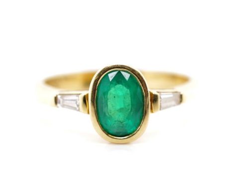 Emerald and diamond set 18ct yellow gold ring with an oval cut emerald in a bezel setting and two accompanying tapered baguet