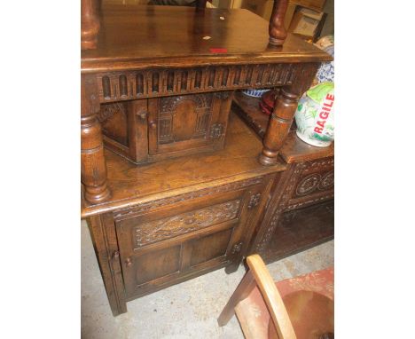 An oak carved court cupboard, the top with moulded edge above a frieze of carved architectural arches, supported on turned co