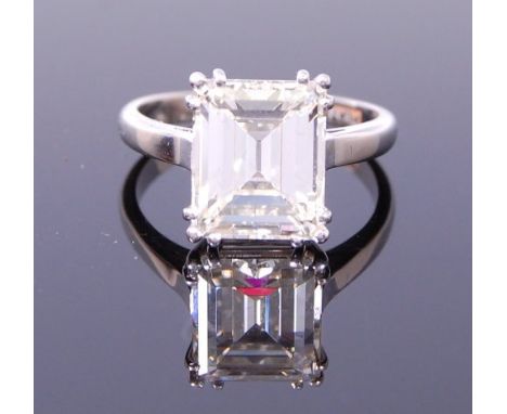 A platinum diamond single stone ring, the emerald cut diamond in a triple four claw setting with squared shoulders, to a D-sh