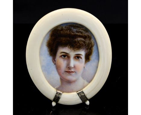 An Edwardian oval portrait miniature of a young lady wearing pearl earrings, on ivory, in a circa 1905 period ivory oval ease