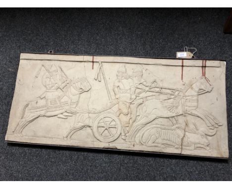 A cast relief panel in metal frame depicting figures on chariot and horseback hunting, 95cm by 43cm.  