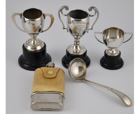 Three silver miniature trophy cups on tuned wooden plinth, a glass spirits flask with silver plated pull off beaker, and a si