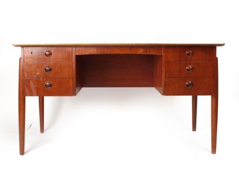 A 1970's teak desk, the rectangular surface above an arrangement of six drawers and having a shelf verso on turned tapered le