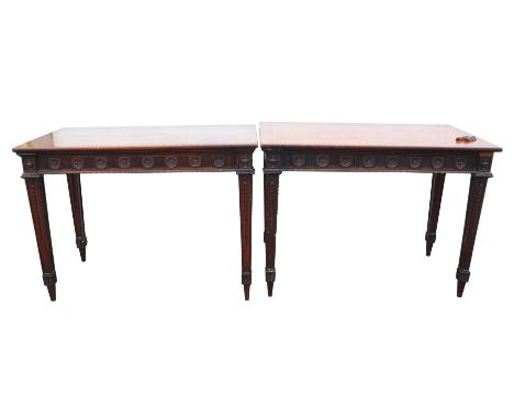 A pair of George III mahogany console tables, 1800s, the banded tops above a fluted and paterae carved frieze, the square tap