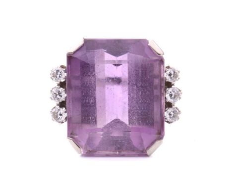 An amethyst and diamond cocktail ring featuring a large emerald-cut amethyst measuring 21.8mm x 18.4mm x 12.7mm, between rows