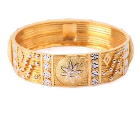 An Indian closed bangle, of geometrical design, with applied motifs on grooved ground, yellow metal testing 22ct, 1.9 cm wide