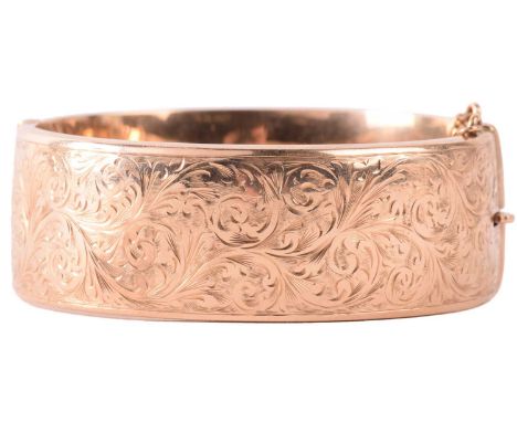 A 9ct yellow gold hinged bangle, half of the hollow bracelet is chased with scrolled acanthus foliage, completed with a conce
