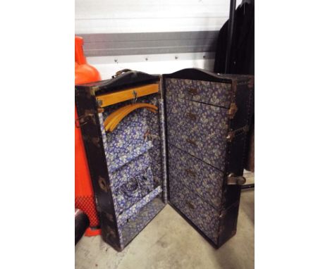 An early 20thC metal bound shipping trunk the interior fitted with five graduated drawers, Bentwood coat hangers and pocket