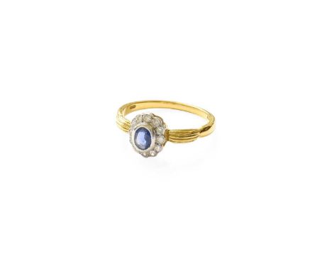 An 18 Carat Gold Sapphire and Diamond Cluster Ring, the oval cut sapphire in a white rubbed over setting, within a border of 