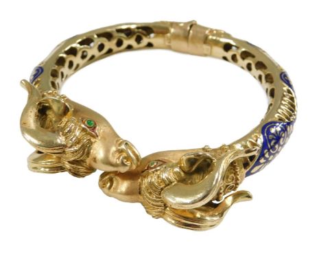 A gold and champleve enamel bangle, with ram's head terminals, the eyes set with cabochon emeralds, with a hinged mechanism, 