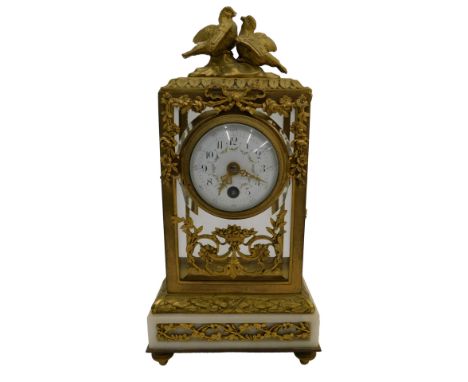 A late 19thC French ormolu and white onyx mantel timepiece, the four glass case decorated with a crest of birds, above a whit