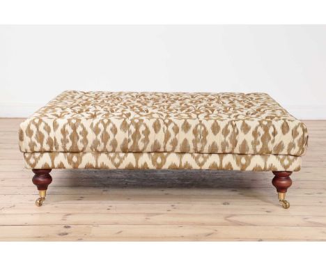 A button-upholstered ottoman, 20th century, with ikat-printed fabric, raised on turned supports and brass castors, 120cm squa