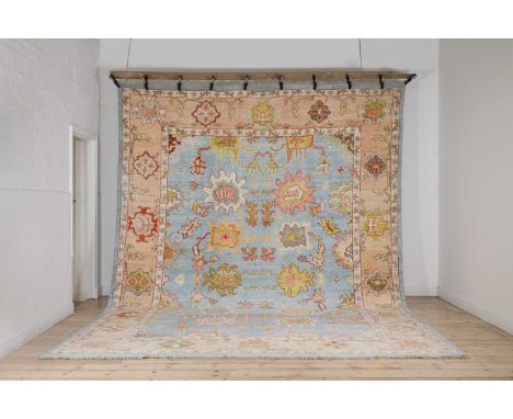 A large Oushak wool carpet, of recent manufacture, Iranian, woven with bold floral motifs to a pastel-blue ground,431 x 320cm