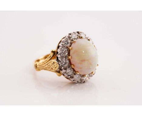 An opal and diamond entourage ring in 18ct gold, centred with a precious opal cabochon of 12.8 x 10.6 mm and a high dome, dis