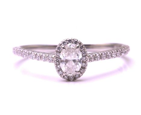 A Tiffany &amp; co. diamond set halo ring, featuring a central oval cut diamond measuring 5.9x3.8mm surrounded by round brill