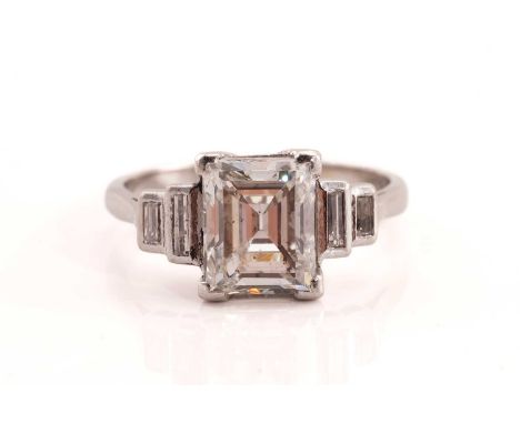An Art Deco style diamond engagement ring, central baguette-cut diamond approximately measuring 8.45 x 6.95 x 4.45 mm, flanke