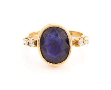 A glass-filled sapphire and diamond ring in 18ct yellow gold, consisting of an oval faceted glass-filled sapphire of 12.2 x 9