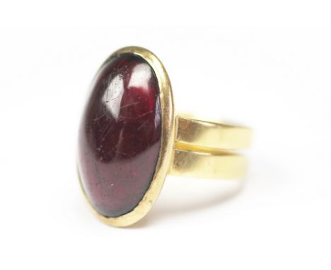 A cabochon garnet ring, the central oval foiled back garnet set within yellow metal roll over surround with double hoop, unma