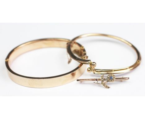 A yellow metal hinged bangle, of plain form, with integral clasp and attached safety chain, stamped '9ct', 10.4gms, and a fur
