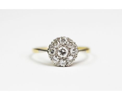 A diamond set cluster ring, the nine stone diamond circular cluster all set in white metal to the tapering shoulders and plai