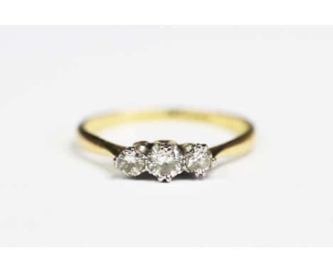 A three stone diamond ring, the three graduated diamonds each claw set in white metal to the tapering shoulders and plain yel