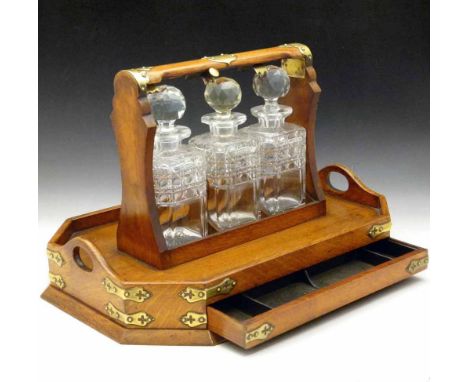 Late Victorian pale oak tantalus with applied Gothic brass mounts, of three square cut glass decanters on an elongated octago