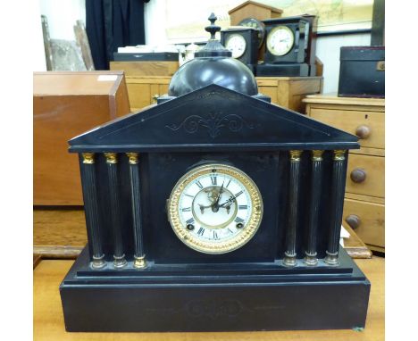 A late Victorian black slate cased mantle clock of architectural form; the movement faced by a white enamelled Roman dial, on