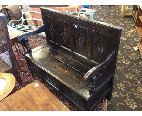 A 17th century style oak monk's bench with lift-top seat and carved four panel back.