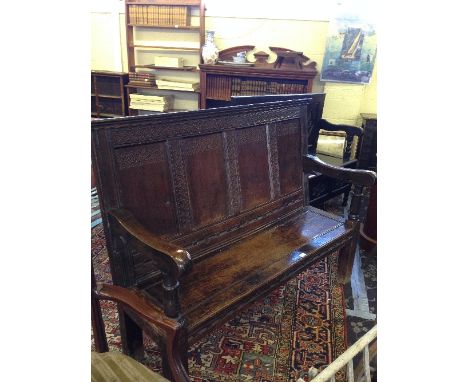 A 17th century style oak bench with carved four panel back, resting on heavy square supports.