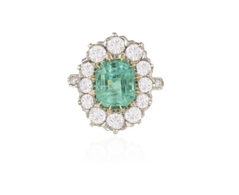 AN EMERALD AND DIAMOND CLUSTER RING The cut-cornered rectangular-cut emerald weighing approximately 2.70cts, within a brillia