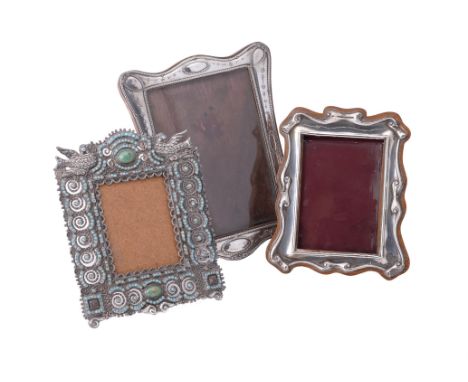 
	
		Three silver or silver coloured photograph frames: Edwardian shaped rectangular with paper scroll design by H. Solomon, 