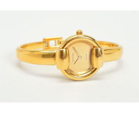 A GUCCI LADIES BANGLE WRISTWATCH, plain circular champagne dial in a gold-plated on stainless steel case on a plain hinged ba