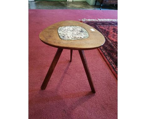 A 1962 elm seated three legged stool, the centre with a ceramic tile, the underside indistinctly inscribed