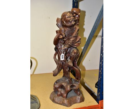 A 20TH CENTURY CHINESE CARVED HARDWOOD FIGURE OF A JOVIAL MAN, holding a staff in both hands, a stylised Cockeral at his feet