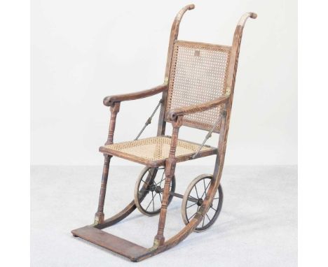 A 19th century ash cane seated folding wheelchair, bearing a label for John Ward Ltd, 246 Tottenham Court Road