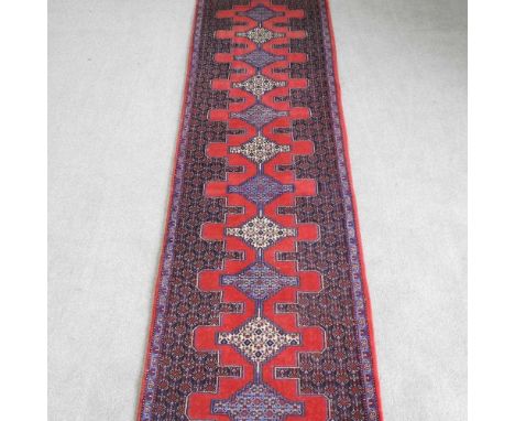 A Persian Senneh runner, having a row of central medallions, on a red ground, 315 x 80cm
