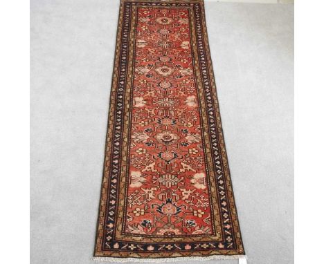 A Persian hamadan runner, with hooked medallions, on a red field, 295 x 100cm