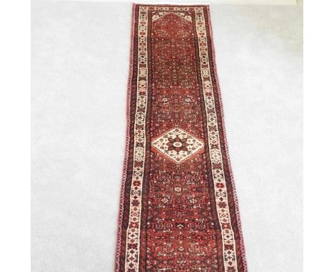 A Persian runner, with foliate designs on a red ground, within multiple borders, 395 x 75cm
